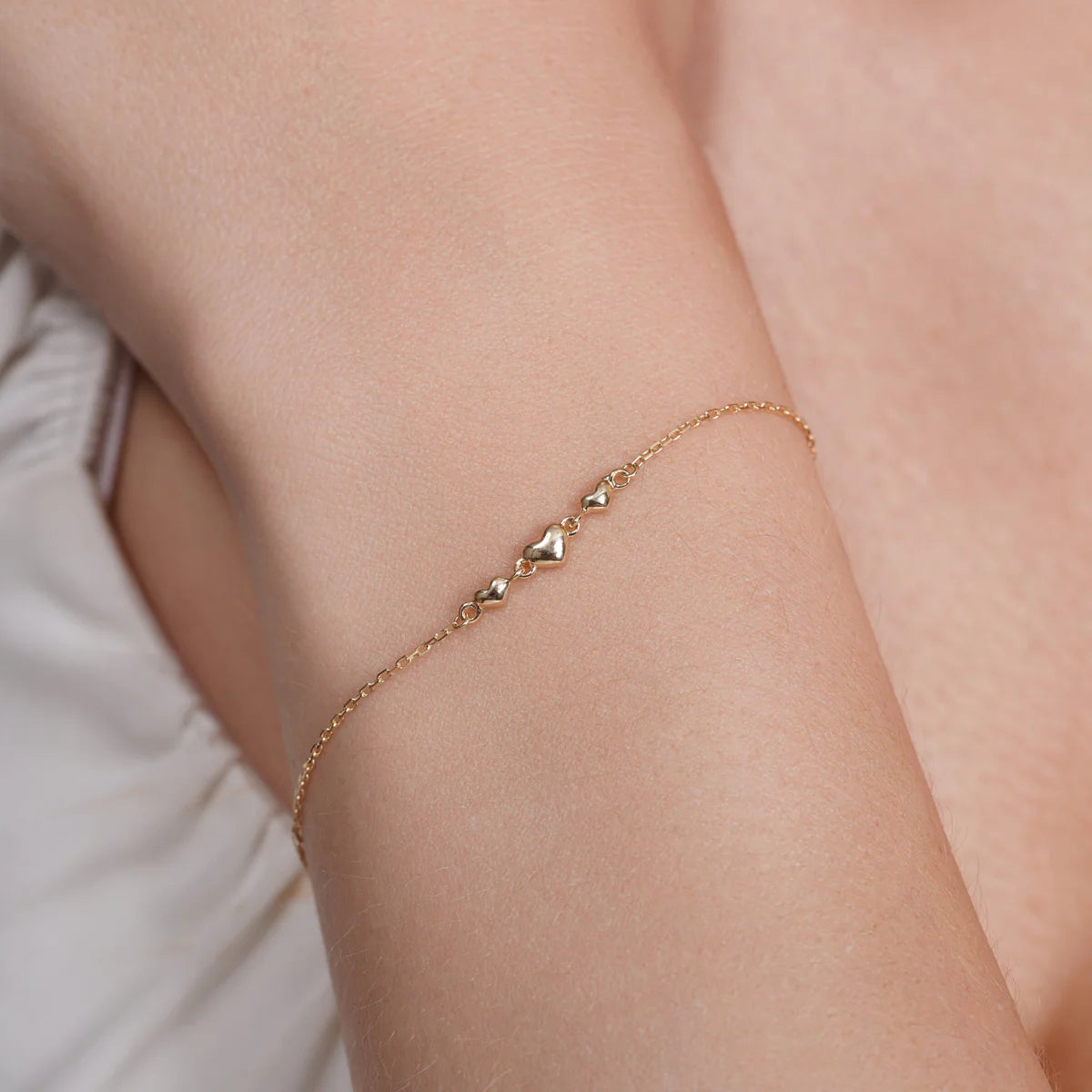 14 karat gold triple heart charm bracelet shown worn on the wrist